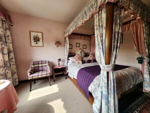 Ein Schlafzimmer mit Himmelbett, einem Sessel, einem kleinen Tisch und einer Lampe.