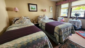 Een hotelkamer met twee bedden, een kleintje tafeltje met een vaas, en een raam met gordijnen.