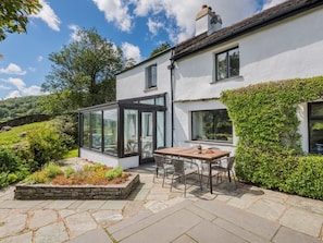 A modern house with a glass conservatory, a stone patio, and a dining area. - 4 Bed in Broughton-in-furness (oc-sz183) (Ulpha)