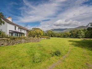 A house with a stone wall, a grassy yard, and a mountain in the background. - 4 Bed in Broughton-in-furness (oc-sz183) (Ulpha)