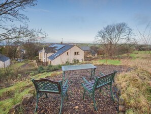 A house with a sloped roof, a garden with a metal table and chairs, and a view of the surrounding landscape. - 2 Bed in Whitehaven (oc-sz216) (Low Moresby)