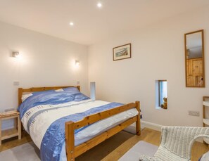 A bedroom with a wooden bed, bedside tables, a chair, a small window, and a mirror on the wall. - 2 Bed in Whitehaven (oc-sz216) (Low Moresby)