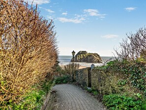 A paved pathway leading to a coastal area with a historic building on a cliff. - 4 Bed in Tenby (oc-fb007) (Tenby)