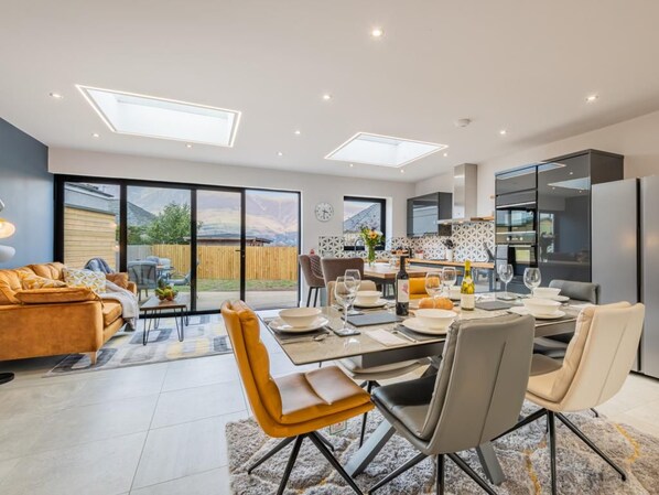 A modern kitchen with a dining area, large windows, and a view of the outdoors. - 3 Bed in Keswick (oc-sz407) (Portinscale)