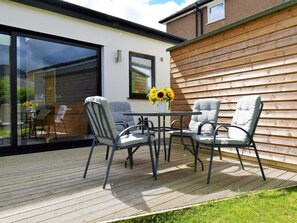 An outdoor patio with a table and four chairs, a wooden deck, and a glass door leading to a garden. - 3 Bed in Keswick (oc-sz407) (Portinscale)