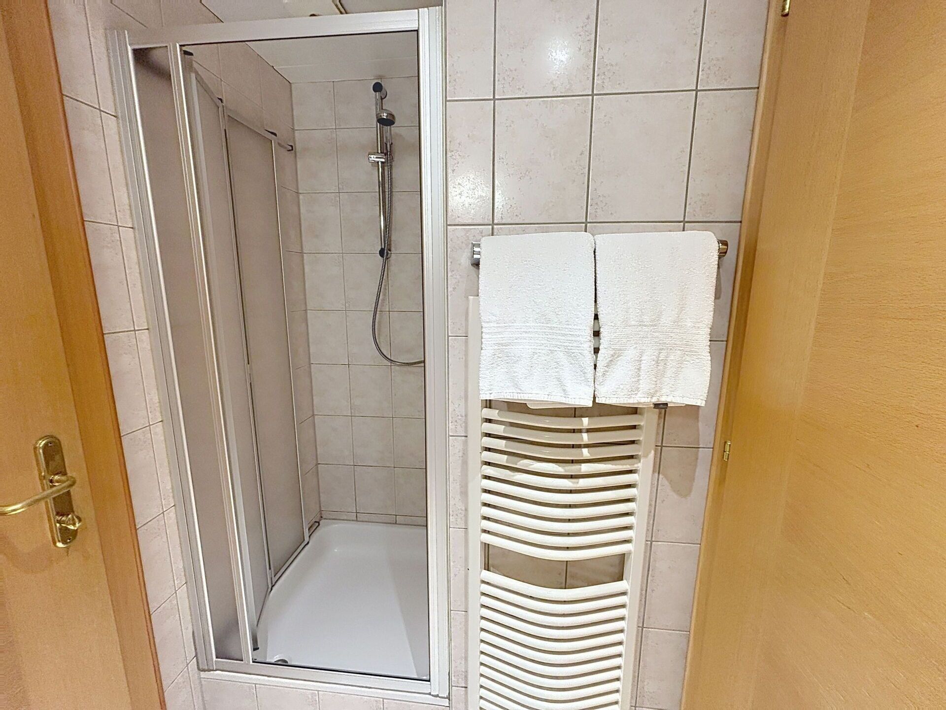 A shower with a glass door, a towel rack with folded towels, and a tiled wall.
