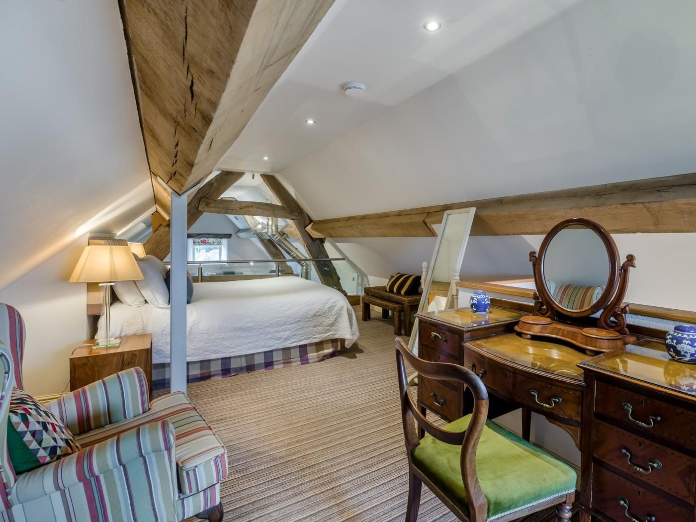 A bedroom with a sloped ceiling, a bed, a dresser, a chair, and a mirror.
