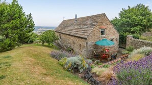 Una casa de piedra con techo inclinado, una ventana pequeña y un patio con muebles de exterior.