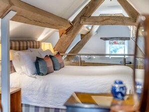 Un dormitorio con techo inclinado, una cama con muchos almohadones, una lámpara de noche y vistas al exterior a través de una ventana.