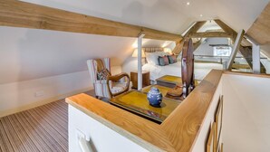 Un dormitorio acogedor en el ático, con techo inclinado, una silla de madera, una mesita de noche con un florero y una cama con almohadas.