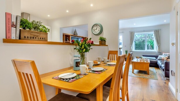 Un coin repas avec une table en bois dressée pour quatre personnes, entourée de chaises. Une horloge est fixée au mur au-dessus de la table.