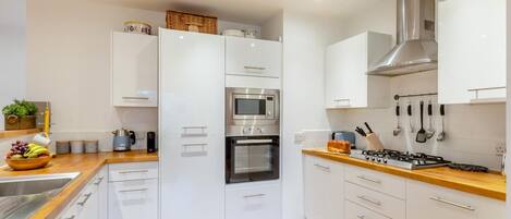 A modern kitchen with white cabinetry, a stainless steel range hood, and a wooden countertop.
