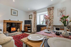 Ein gemütliches Wohnzimmer mit Kamin, einem für zwei Personen gedeckten Esstisch und einer bequemen Couch.