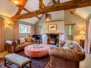 A cozy living room with a fireplace, leather sofas, a round ottoman, and a patterned rug.