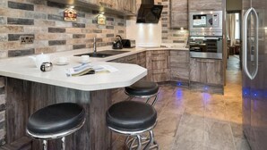 A modern kitchen with a stone backsplash, wooden cabinets, a built-in oven, and a stainless steel refrigerator. - 3 Bed in Keswick (oc-sz574) (Keswick)