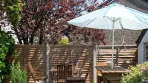 A wooden deck with outdoor furniture, a pergola with a white umbrella, and a garden with various plants. - 3 Bed in Keswick (oc-sz574) (Keswick)