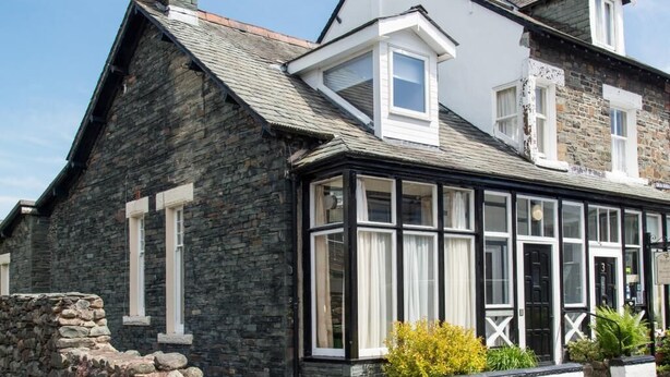 A stone building with a black-framed glass extension, a stone wall, and a small garden area. - 3 Bed in Keswick (oc-sz574) (Keswick)