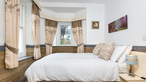 A bedroom with a bed, curtains, a nightstand, a lamp, and a painting on the wall. - 3 Bed in Keswick (oc-sz574) (Keswick)