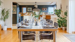 A dining area with a wooden table set for six, surrounded by chairs, with a kitchen in the background. - 4 Bed in Wembury (oc-54383) (Wembury)