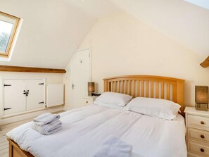 Quarto com cama de madeira, paredes brancas, claraboia, radiador e guarda-roupa.