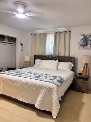 Quarto com cama, duas mesas de cabeceira, ventoinha no teto e janela com cortinas.