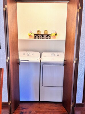 A laundry room with two white washing machines and a shelf above containing decorative items.