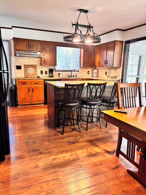 A kitchen with wooden cabinets, a central island with stools, a chandelier, and a large window.