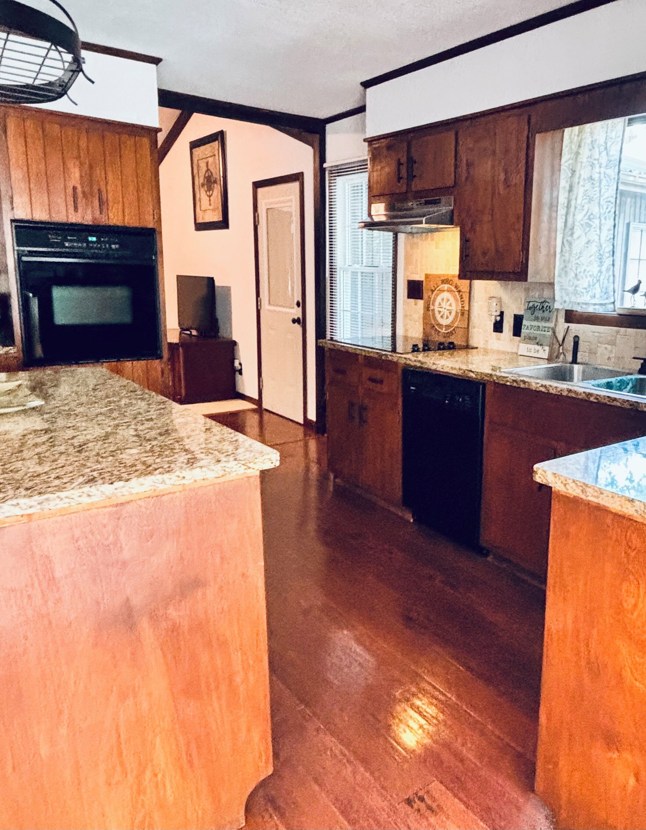 A kitchen with wooden cabinets, a granite countertop, a dishwasher, and a window with blinds.