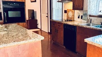 A kitchen with wooden cabinets, a granite countertop, a dishwasher, and a window with blinds.