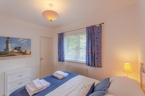 A bedroom with a bed, a nightstand, a lamp, a window with curtains, a door, and a painting on the wall. - 2 Bed in Aberdyfi (oc-dy028) (Aberdovey)