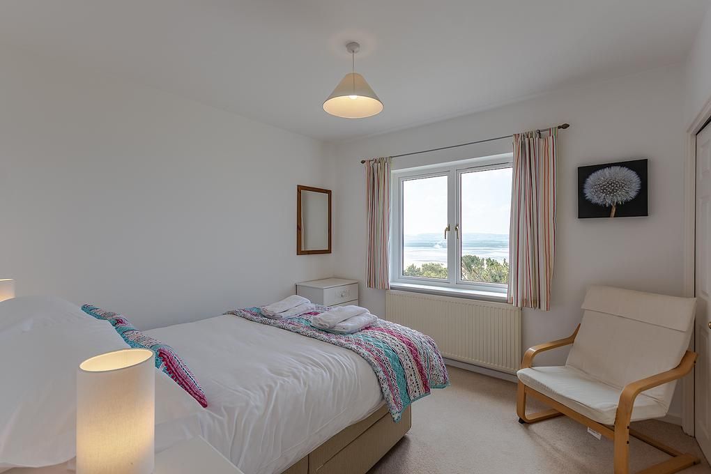 A bedroom with a bed, a chair, a window with curtains, a picture on the wall, and a lamp.
