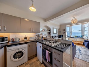 A modern kitchen with a built-in washing machine, a gas stove, and a large window overlooking the sea.