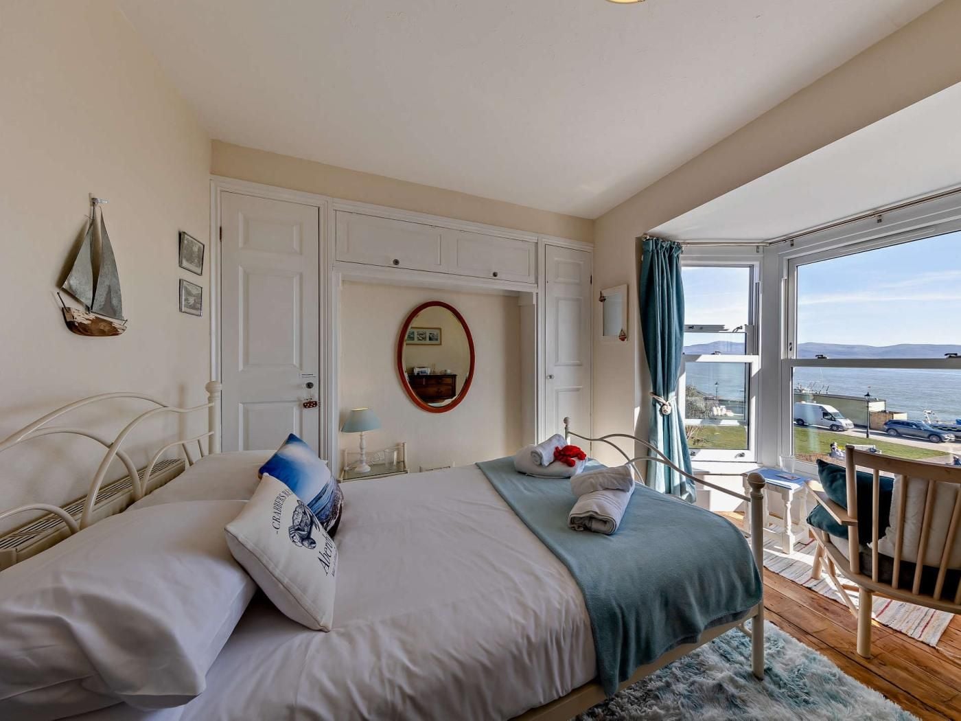 A bedroom with a bed, a chair, a table, a window with a view of the sea, and a door.