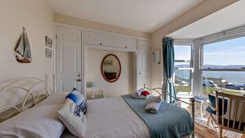 A bedroom with a bed, a chair, a table, a window with a view of the sea, and a door.