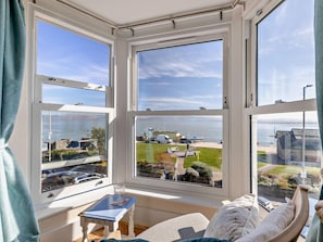 A room with a bay window overlooking a marina with boats and a clear sky.