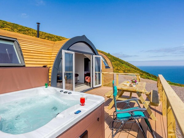 A cozy outdoor hot tub area with a wooden deck, a table, and a chair.