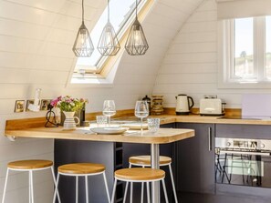 A modern kitchen with a skylight, wooden bar stools, and a dining area with a table set for two.