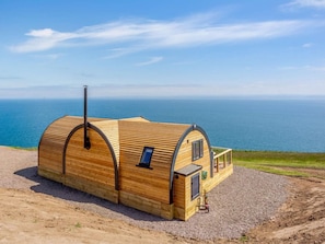 A wooden cabin with a curved roof, a small balcony, and a view of the sea.
