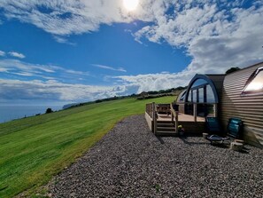 A modern house with a curved glass extension, a gravel driveway, and a grassy field.