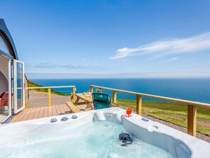 A hot tub with a view of the ocean, a wooden deck, and a table with chairs.