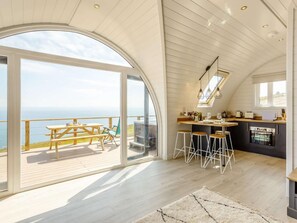 A modern kitchen with a bar area, large windows, and a view of the sea.