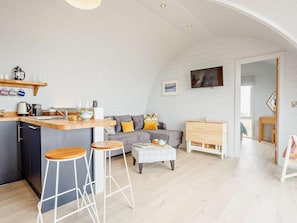 A modern kitchen with bar stools, a grey sofa with yellow cushions, and a wooden dining table.