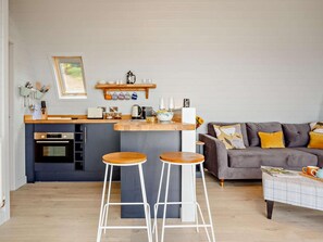 Une cuisine moderne avec un îlot central, des tabourets de bar, un canapé gris et une table basse.