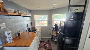 A kitchen with a wooden countertop, white cabinets, a black refrigerator, and a window with a view of greenery.