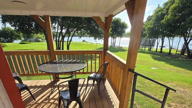 A wooden deck with a table and chairs, overlooking a grassy area and a body of water.