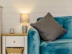 Un canapé de couleur turquoise avec un coussin gris, une lampe de chevet, un haut-parleur Sony et un panier en osier placé sous le tiroir.