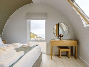 Une chambre à coucher avec un lit, un bureau en bois, un miroir et une vue sur l’extérieur.