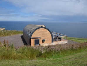 A wooden dome-shaped building with a small porch and a door, situated on a grassy hill overlooking a body of water. - 2 Bed in Tain (oc-81340) (Nigg)