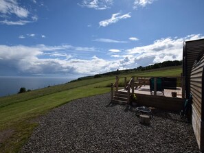 A wooden deck with a view of the sea, a picnic table, and a grill area.