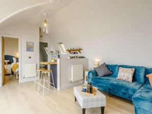 Un salon moderne avec un canapé bleu, une table basse et un coin cuisine doté d’un bar.